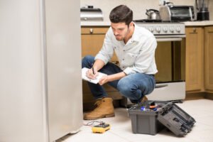 Portrait of a handsome male technician doing a work report on a broken fridge in a home kitchen
